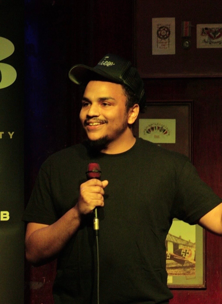 Comedian in black cap holding microphone on stage
